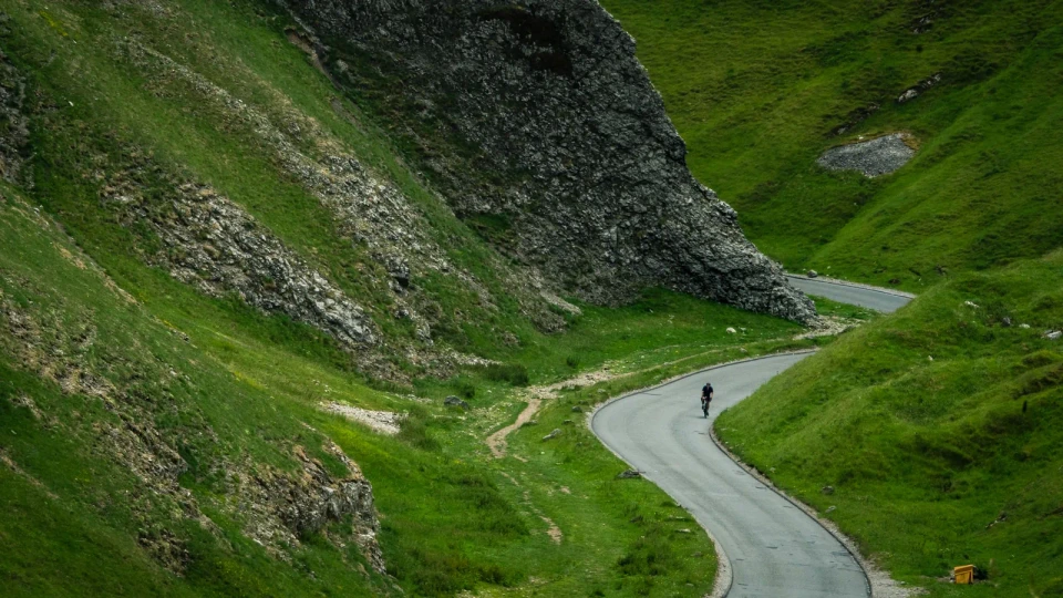 Un ciclista recorre una carretera de montaña: fotografía ambiental de la guía, no una imagen de los modelos comparados